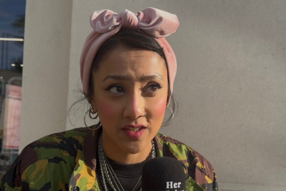 Person holding a microphone with 'Her Window' branding, wearing a camouflage jacket and headband.