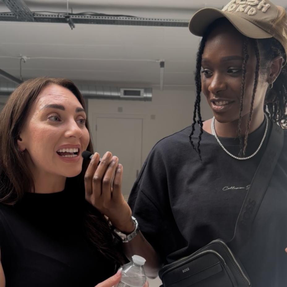 Two women standing together indoors, one holding a water bottle.